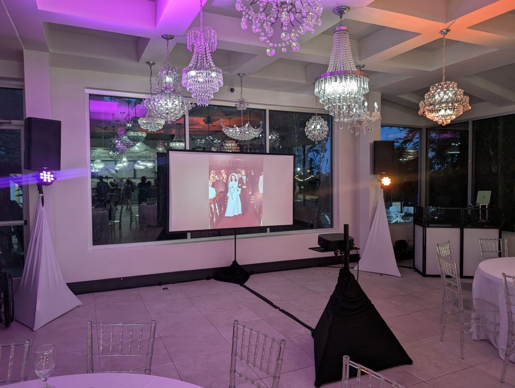 Projection screen showing a photo slideshow in a ballroom with pink uplighting