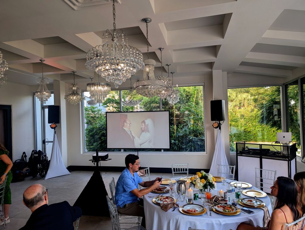Projector screen and speakers set up in a chandelier-lit banquet room