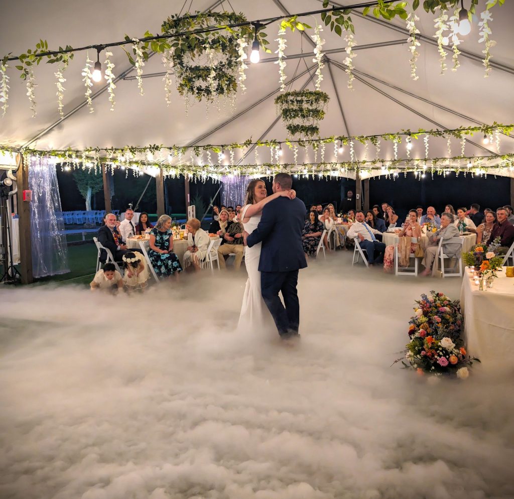 Bride and groom first dance on a cloud of low fog under a tented reception