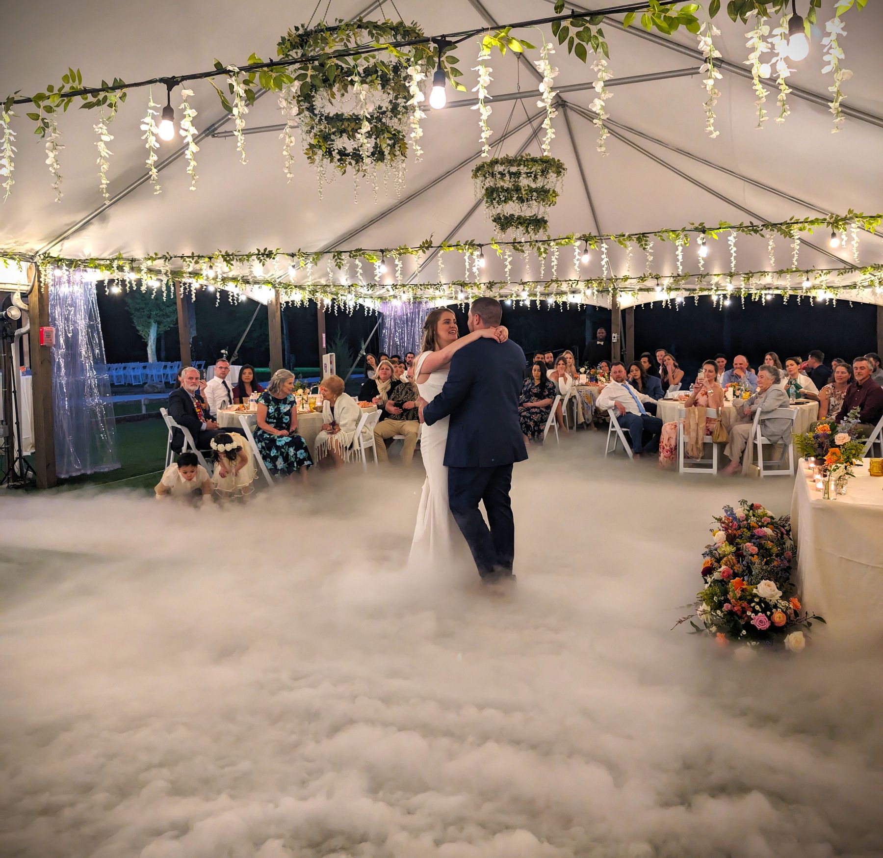 Bride and groom first dance on a cloud of low fog under a tented reception