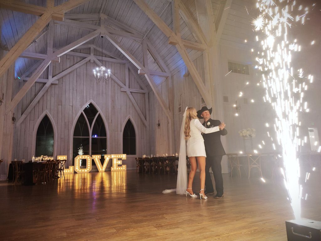 Couple's first dance beside cold spark fountains and lit LOVE marquee letters