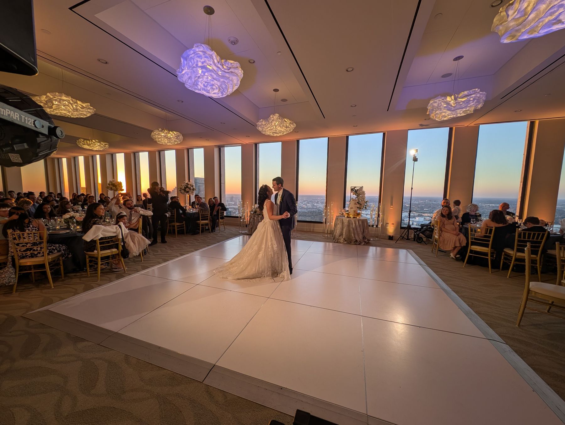 Couple's first dance on a white dance floor beside floor-to-ceiling windows