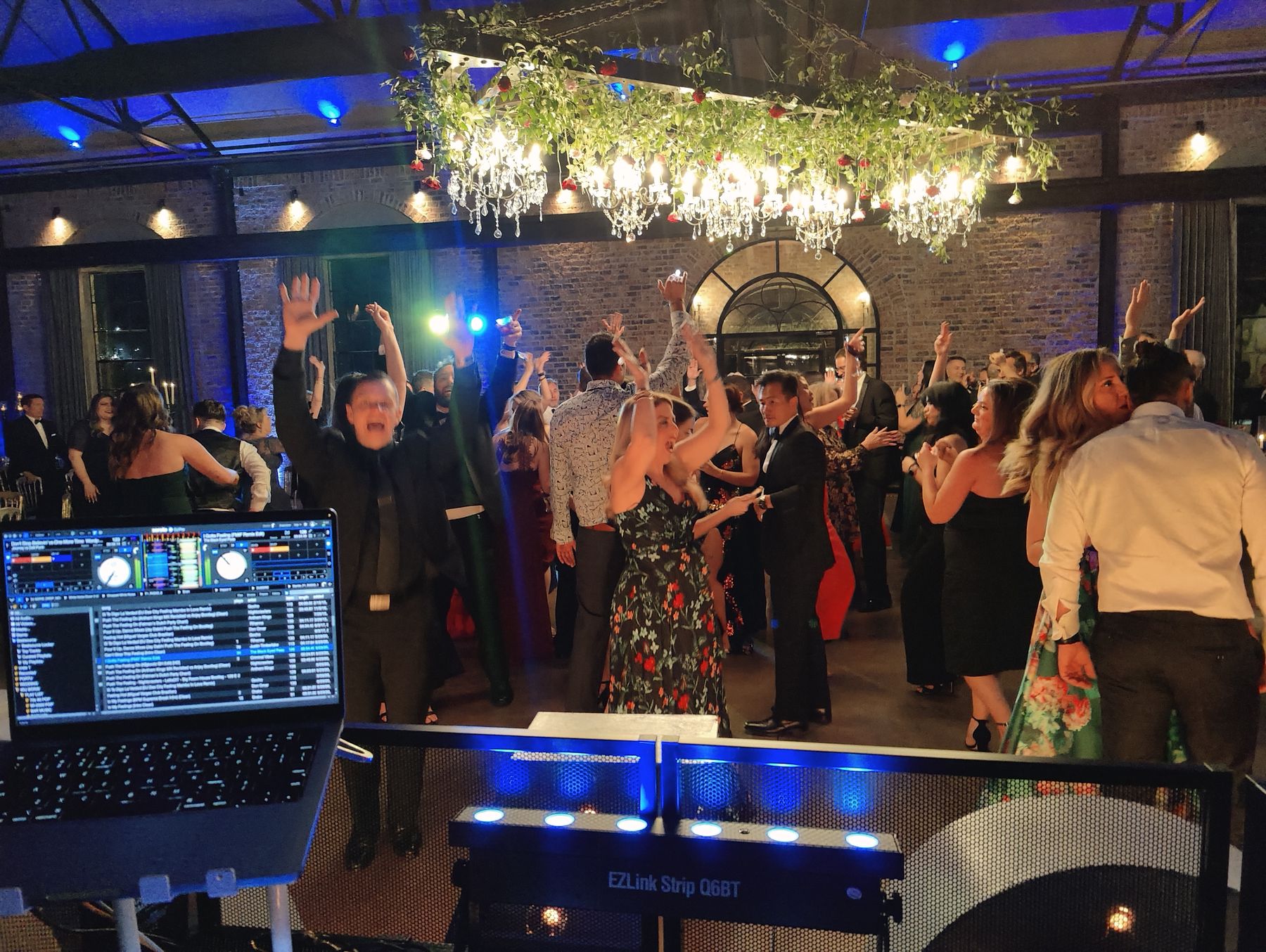 Guests dancing in front of the DJ booth under a floral chandelier