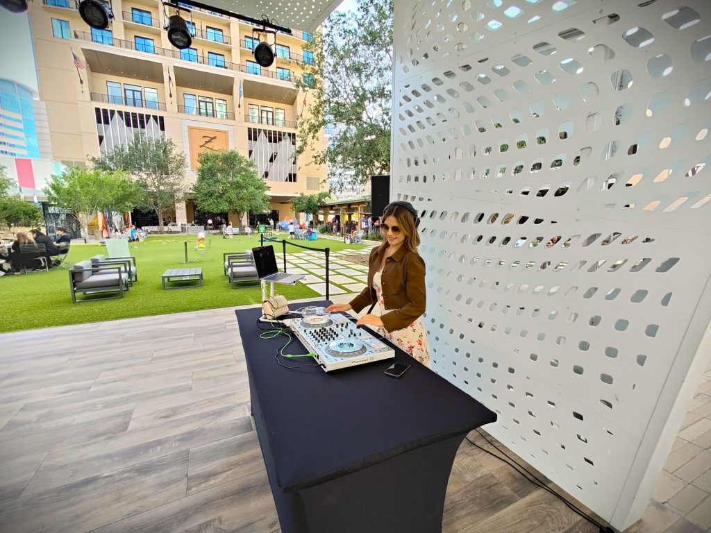 DJ booth set up outdoors on a lawn beside a white decorative screen