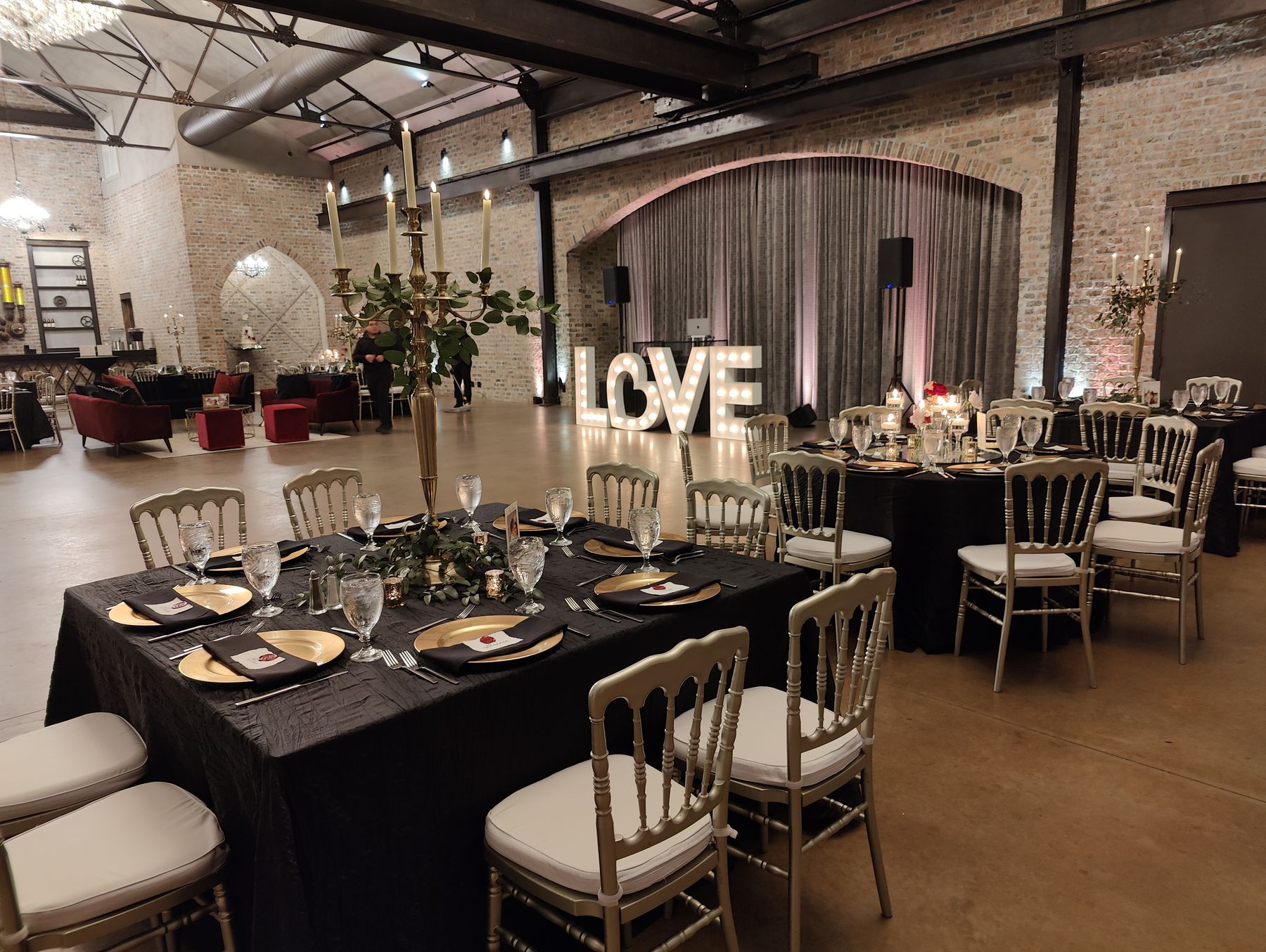 Black-linen reception tables and LOVE marquee letters in an industrial-style venue
