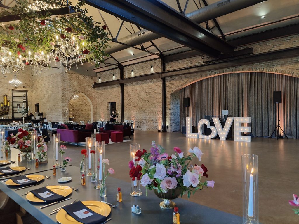 Reception tables with candles and flowers in front of lit LOVE marquee letters