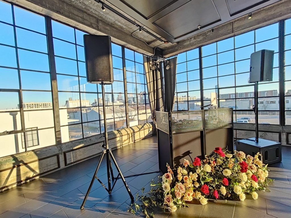 Speakers on stands beside a floral arrangement in a window-lined event space