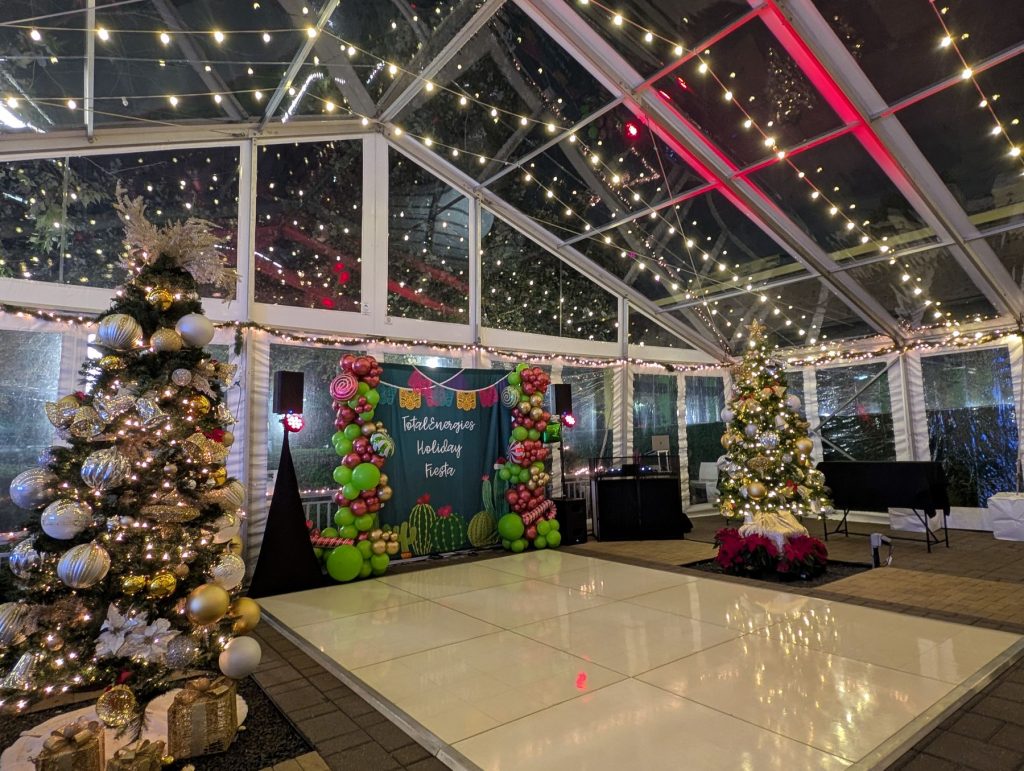 White dance floor inside a clear tent with string lights and Christmas trees